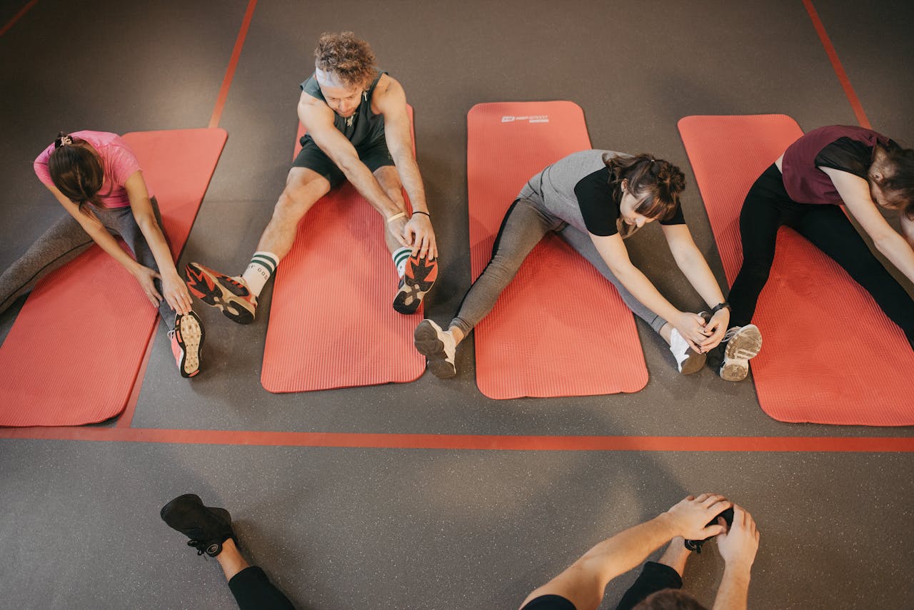 Four people stretching on red mats during a group exercise session indoors.